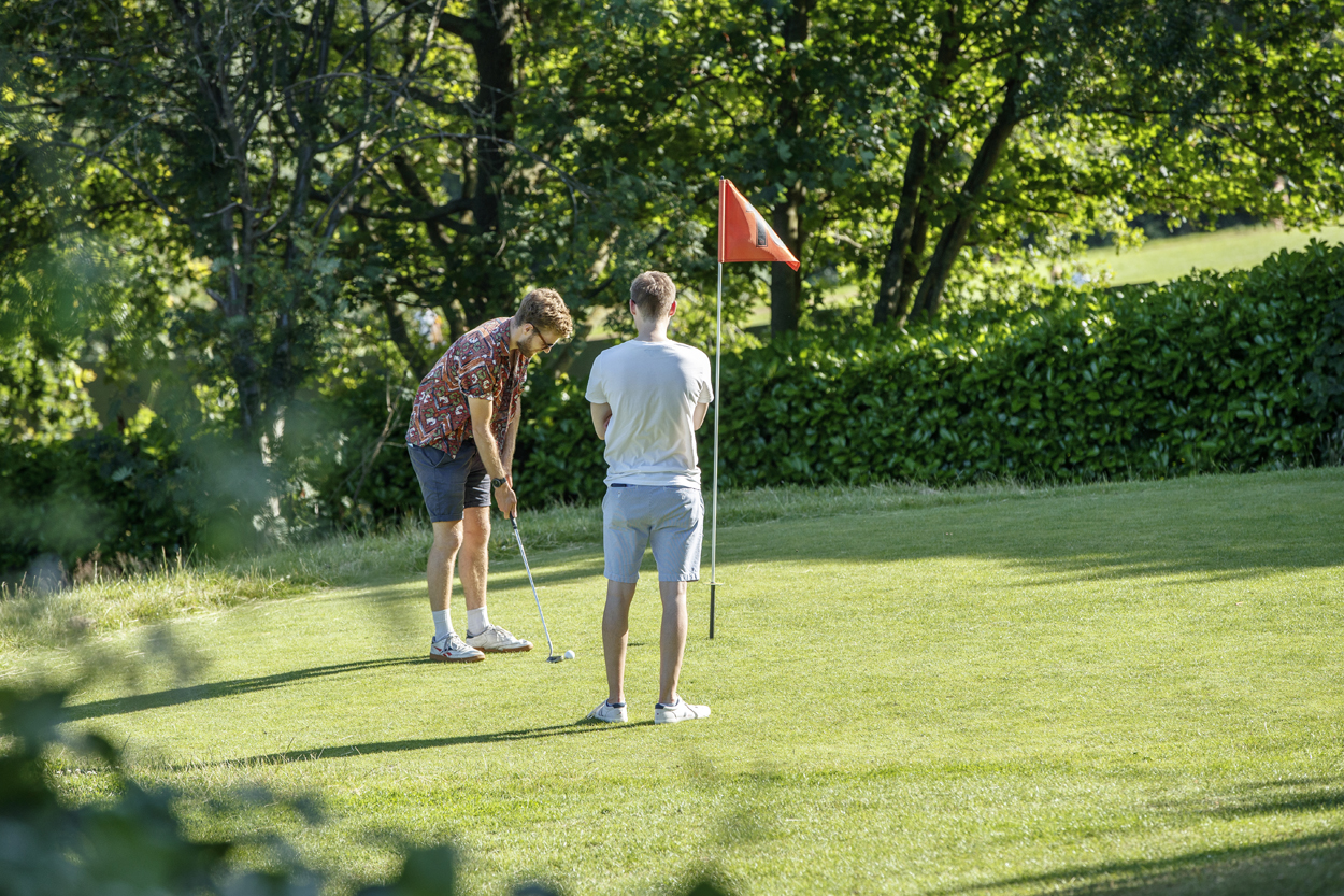 Two people playing pitch and putt on a sunny day.