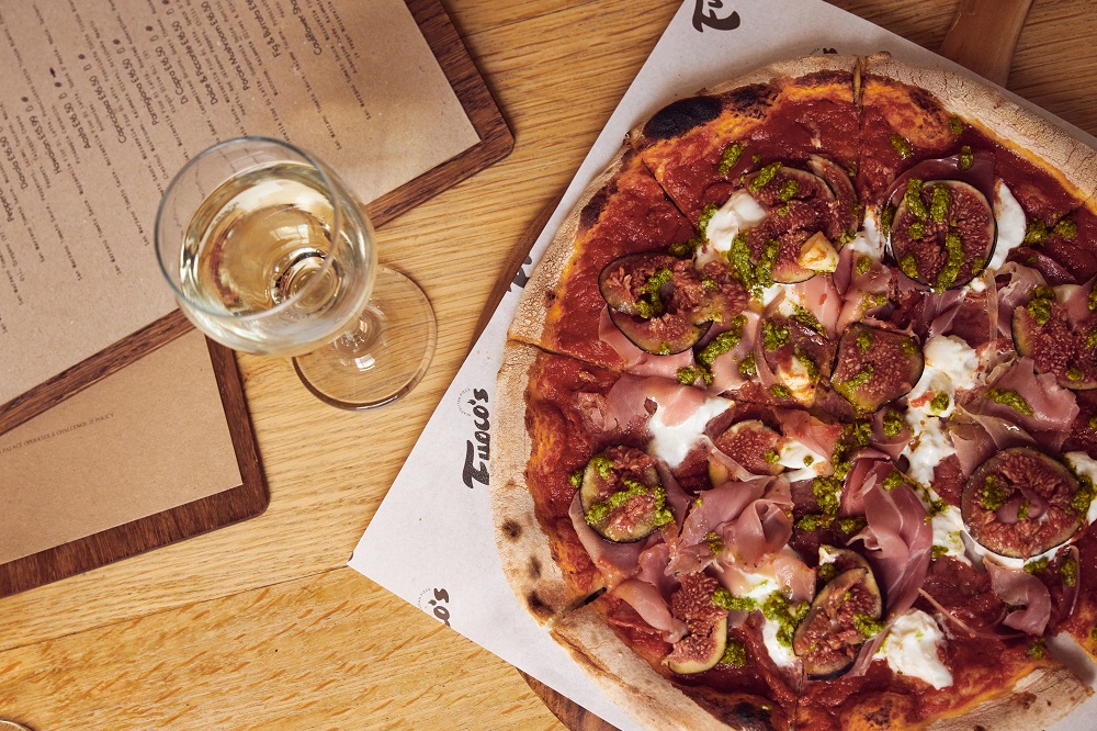 A large pizza with cheese, ham, and figs with a glass of white wine.