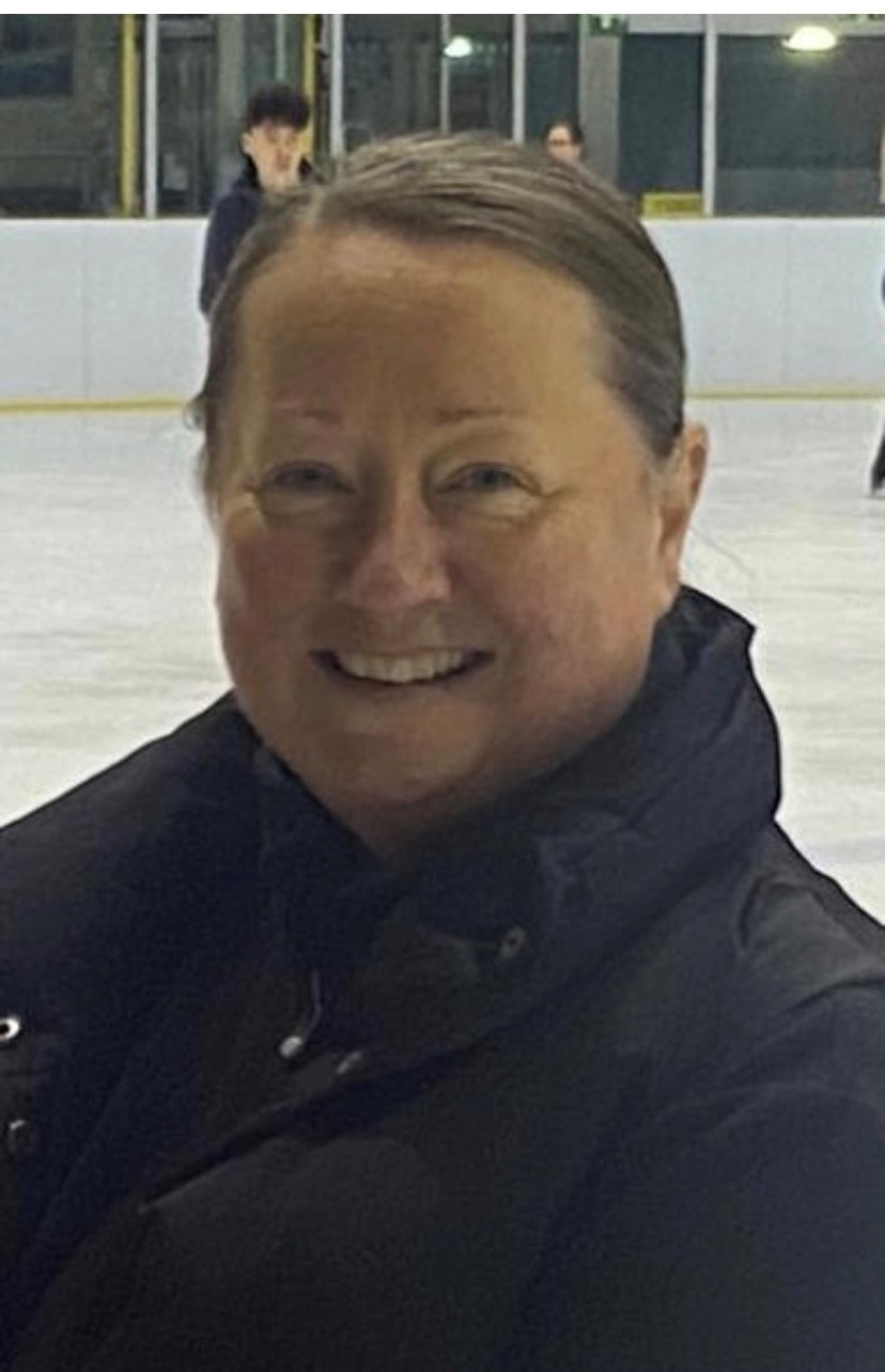 woman in black puffer coat smiles whilst standing on an ice rink