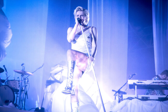Music artist Robyn standing on stage in white at Alexandra Palace.