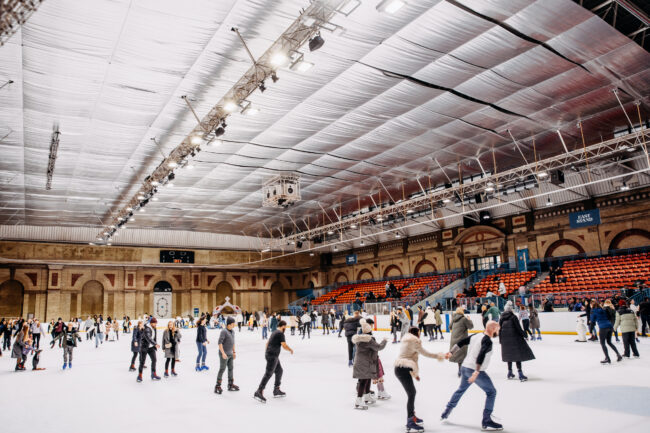 A group of people skating gracefully on an ice rink inside Alexandra Palace.