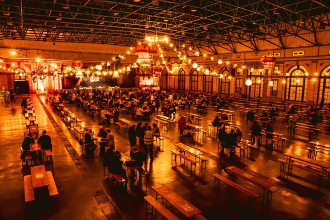 A large hall set up with benches and tables with golden lights.